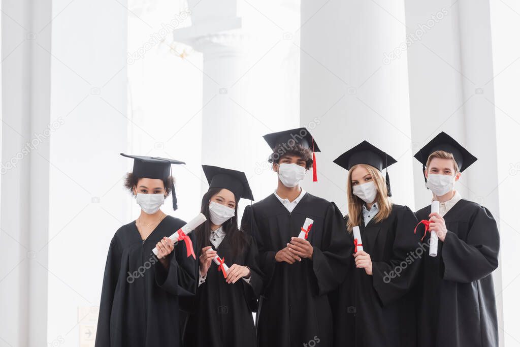 Multiethnic graduates in medical masks holding diplomas 