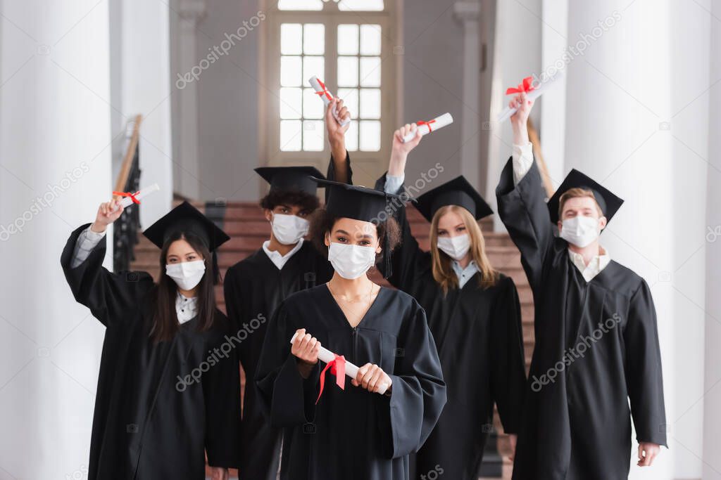 Interracial bachelors in protective masks holding diplomas 