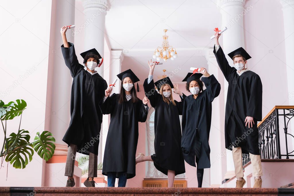 Multiethnic graduates in medical masks rising diplomas in university 