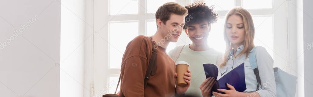 Interracial students with coffee to go and notebook standing near window, banner 