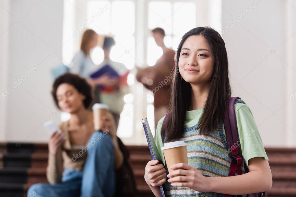 Asian student with coffee to go and notebook in university 