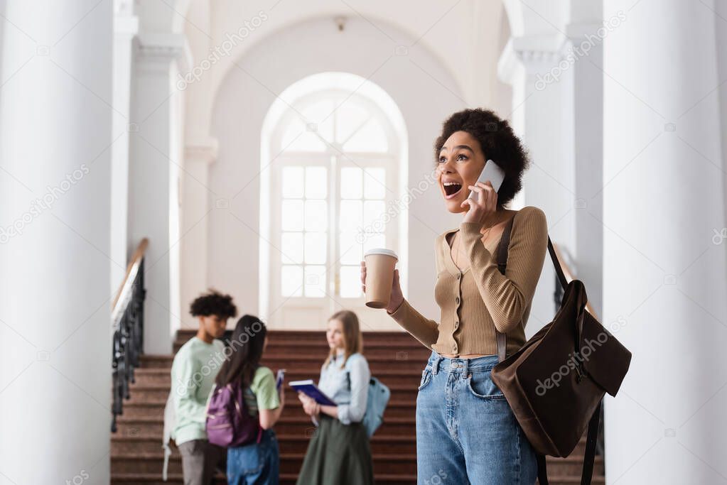 Excited african american student with coffee talking on cellphone 