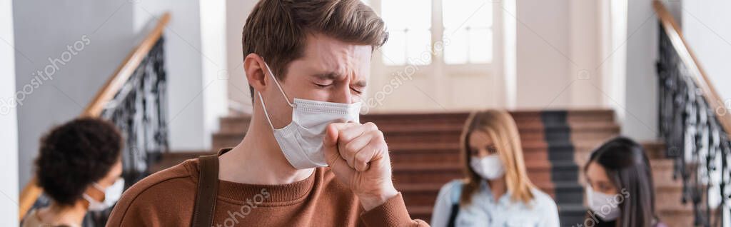 Student in medical mask coughing near multiethnic friends on blurred background, banner 