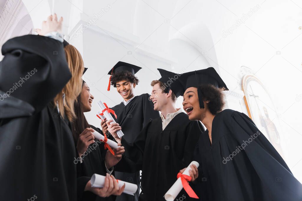 Low angle view of happy multiethnic graduates with diplomas in university hall 