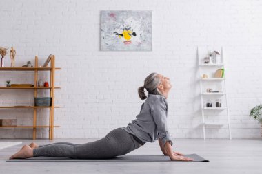 Kobra giymiş orta yaşlı bir kadın evde yoga yapıyor. 