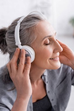 Mutlu orta yaşlı kadın kablosuz kulaklıkla müzik dinliyor. 