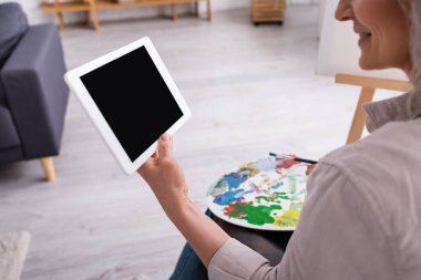 Boş ekranlı palet ve dijital tablet taşıyan mutlu olgun kadın görüntüsü