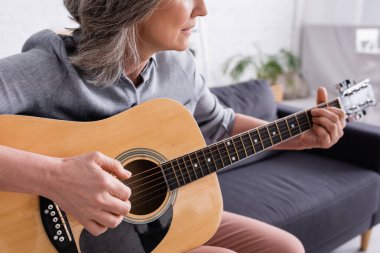 Gri saçlı, akustik gitar çalan orta yaşlı bir kadın. 