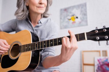 Gülümseyen orta yaşlı kadının oturma odasında akustik gitar çalmasını kısmen görmek