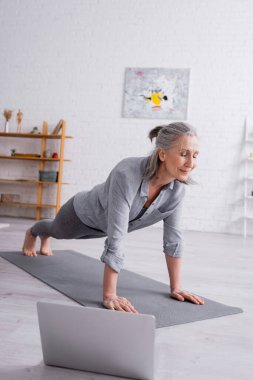 Yetişkin bir kadın dizüstü bilgisayarın yanında spor paspası yapıyor.