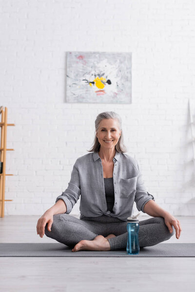 happy middle aged woman sitting in lotus pose on yoga mat 