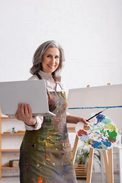 Joyful Mature Woman Holding Palette Laptop Canvas — Stock Photo, Image