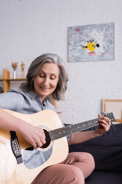 happy middle aged woman with grey hair playing acoustic guitar 