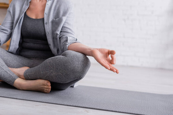 part of mature woman sitting in lotus pose on yoga mat