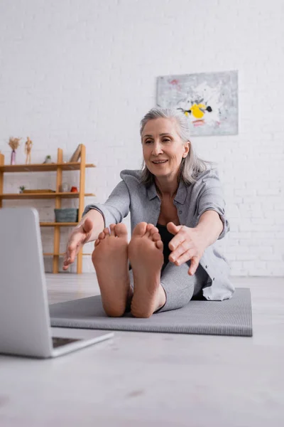 Smiling Mature Woman Grey Hair Stretching Yoga Mat Laptop Blurred — Stock Photo, Image