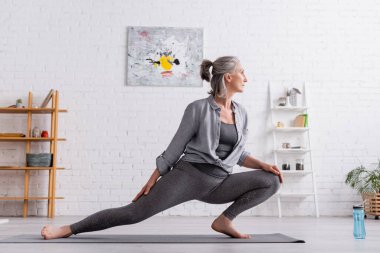 Esnek orta yaşlı bir kadının minder üzerinde yoga çalışmasının yan görünüşü 