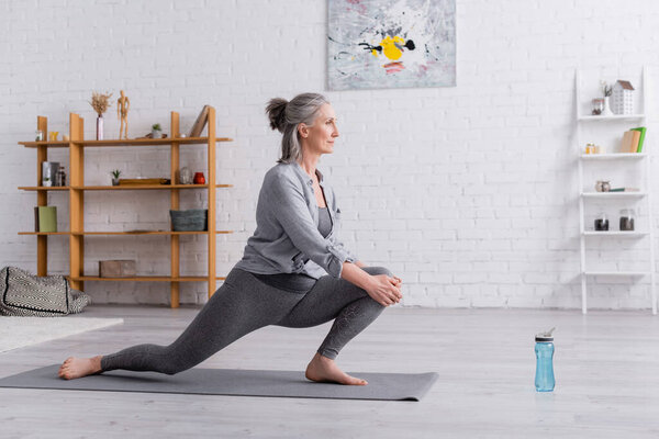 side view of flexible mature woman practicing yoga on mat 