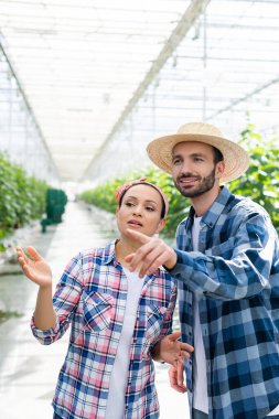 Gülümseyen çiftçi, Glasshouse 'daki Afrikalı Amerikalı meslektaşını parmağıyla işaret ediyor.