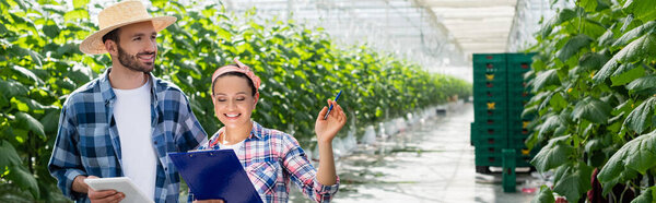 smiling african american farmer with clipboard pointing with hand near colleague with digital tablet, banner