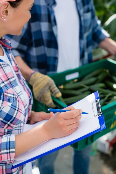 African American Farmer Writing Clipboard Colleagues Box Fresh Cucumbers Blurred — Stock Photo, Image