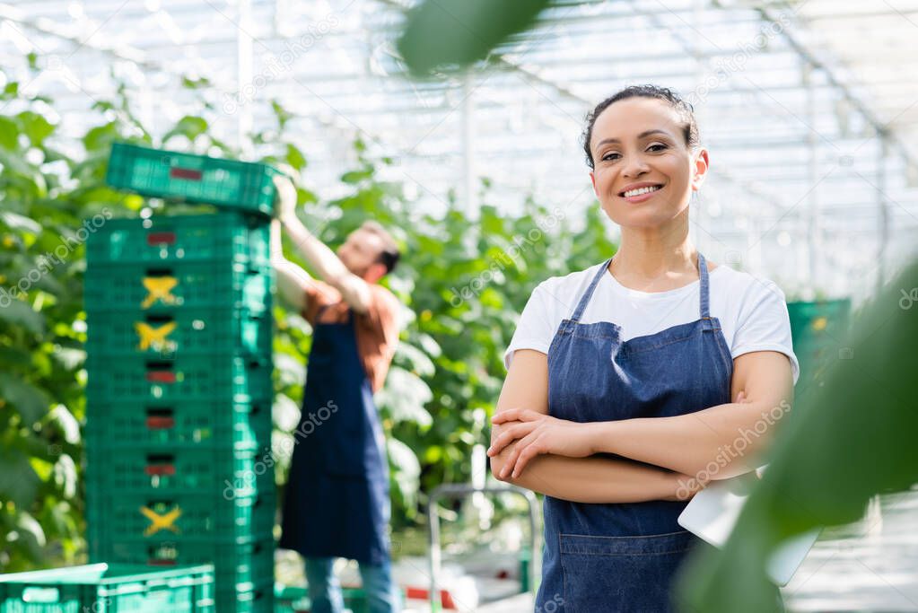 happy african american woman standing with crossed arms near farmer working on blurred background