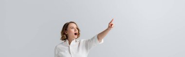 overweight and shocked woman in white shirt pointing with finger isolated on grey, banner clipart