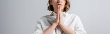 cropped view of young overweight woman in white shirt with praying hands isolated on grey, banner clipart