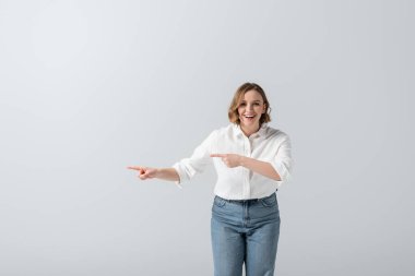 happy overweight woman in jeans pointing with fingers isolated on grey  clipart