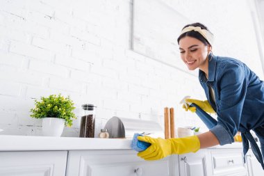 Gülümseyen ev hanımı mutfak atölyesini sünger ve deterjanla temizliyor. 