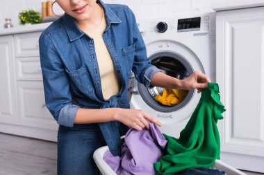 Cropped view of housewife holding colorful clothes in kitchen  clipart
