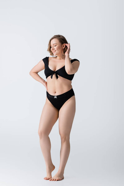 полная длина избыточного веса и босиком молодая женщина позирует с рукой на бедре на белом 