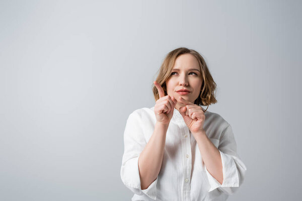 curious overweight woman in white shirt pointing with fingers isolated on grey 
