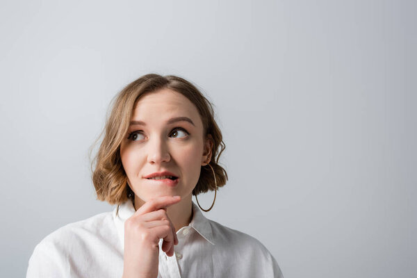 pensive overweight woman in white shirt biting lips isolated on grey 