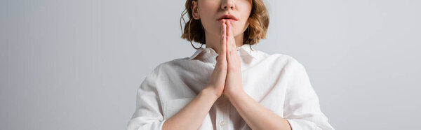 cropped view of young overweight woman in white shirt with praying hands isolated on grey, banner