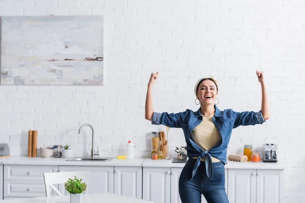 Cheerful housewife showing muscles in kitchen at home