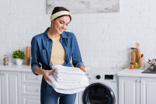 Cheerful housewife in denim shirt looking at white towels 