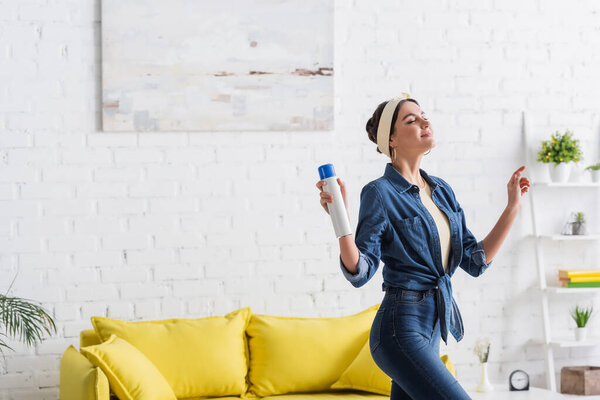 Young woman holding bottle of air freshener at home 