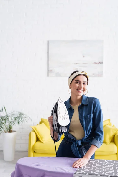 Alegre Ama Casa Sosteniendo Plancha Mirando Cámara Cerca Ropa Bordo —  Fotos de Stock