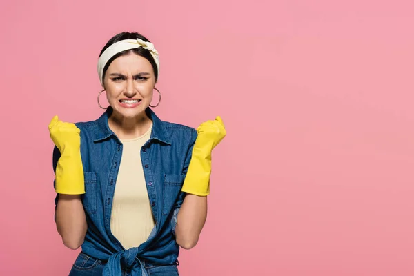 Angry housewife in rubber gloves looking at camera isolated on pink