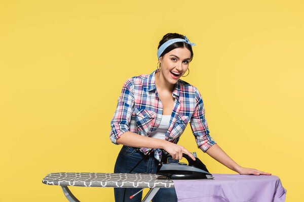 Улыбающаяся домохозяйка гладит одежду изолированную на желтый 