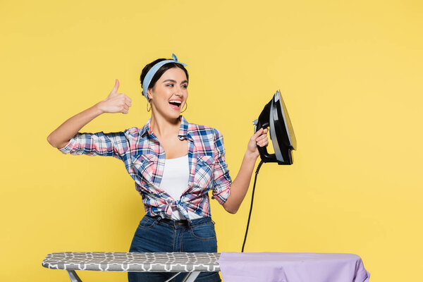 Улыбающаяся женщина с железом показывает, как у доски изолированы на желтый 