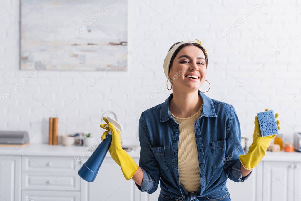 Smiling housewife in rubber gloves holding sponge and detergent 