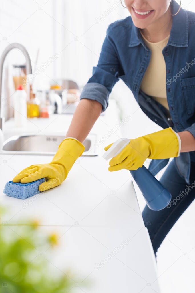 Cropped view of smiling woman cleaning kitchen worktop with detergent and sponge 