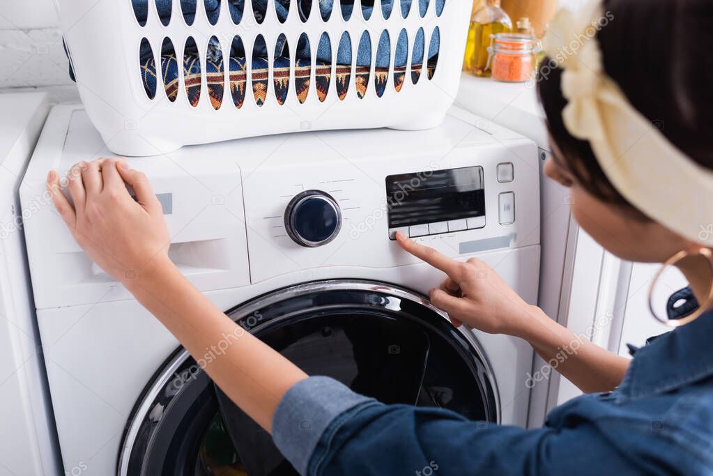 Blurred housewife switching washing machine in kitchen 