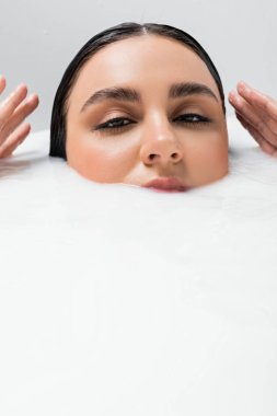 young woman looking at camera while immersing in bath with milk clipart