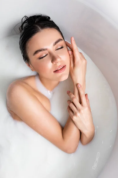 牛乳に浸かりながら顔に触れる若い女性のオーバーヘッドビュー — ストック写真
