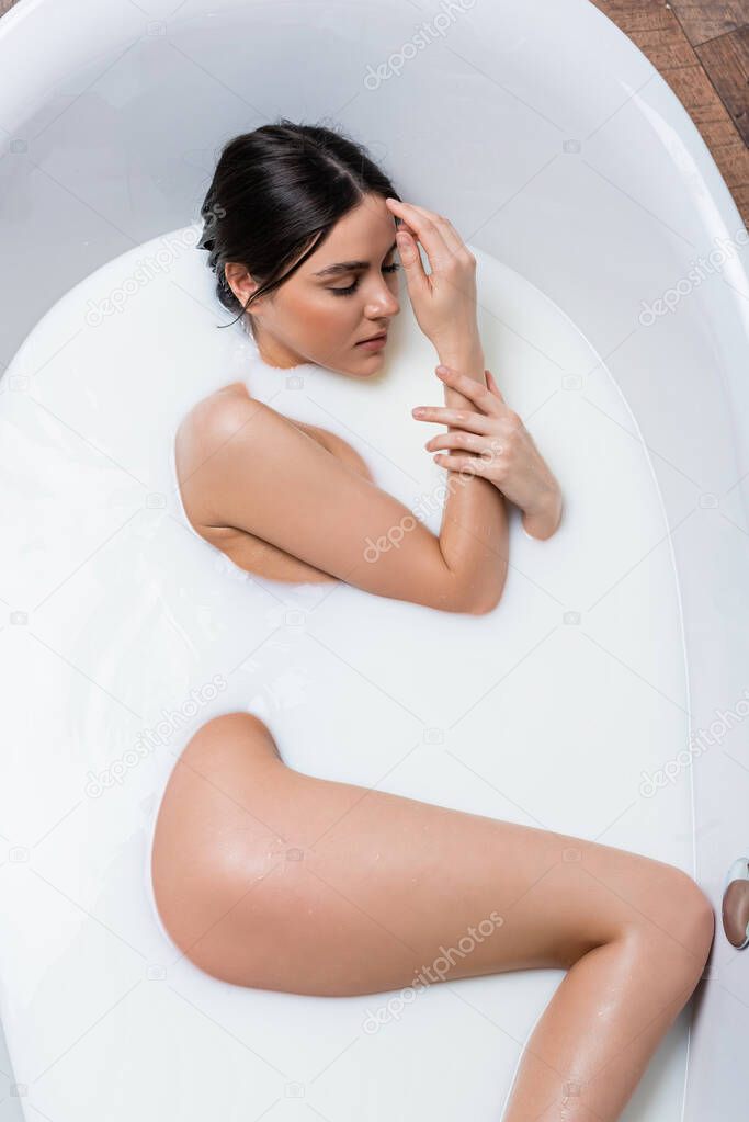 top view of sensual woman with closed eyes taking bath with milk