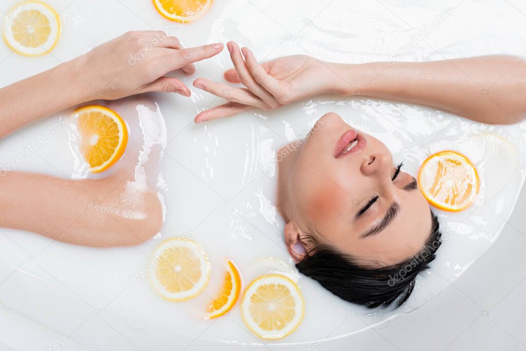 overhead view of young woman relaxing in milky bath with orange and lemon slices