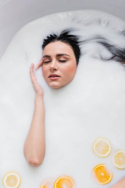 Dilimlenmiş limon ve portakalla süt banyosunda dinlenirken yüzüne dokunan şehvetli kadın.
