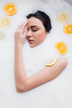 Dilimlenmiş limon ve portakallarla süt banyosunda dinlenirken el ele tutuşan genç kadın.